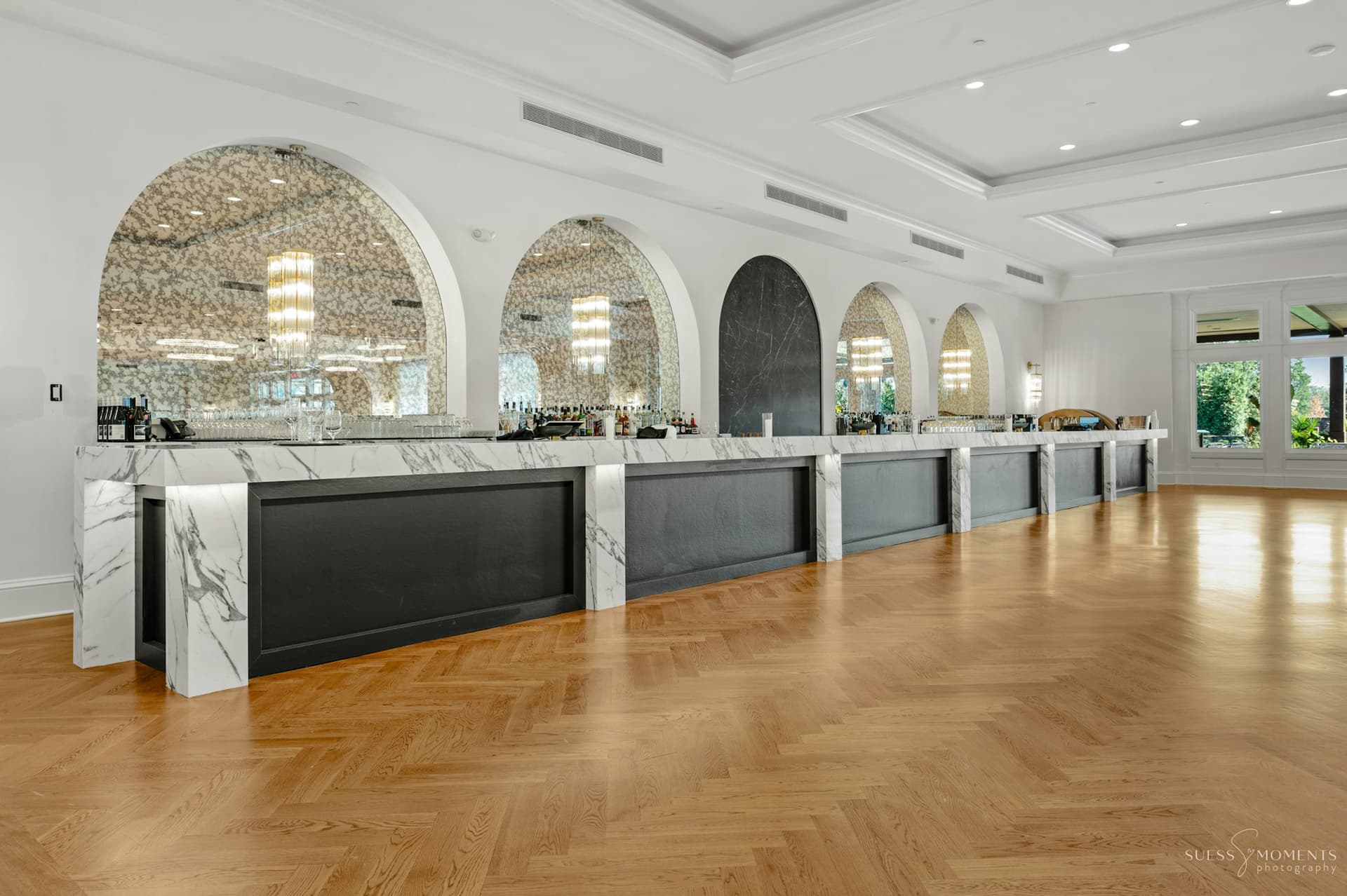 A bright reception hall with arched marble bar stations and herringbone floors at TillingHouse