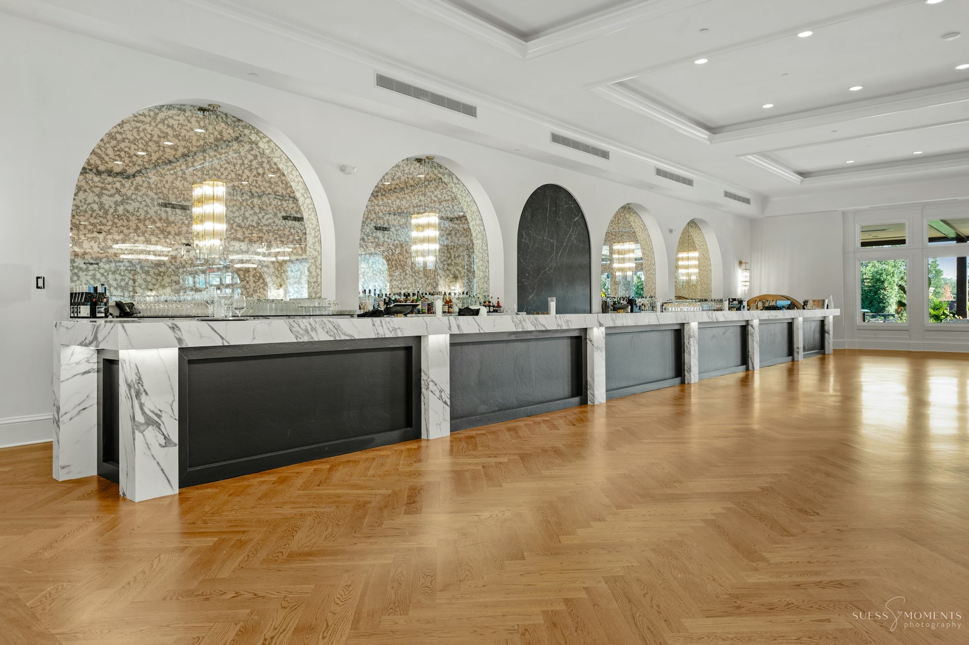 A bright reception hall with arched marble bar stations and herringbone floors at TillingHouse